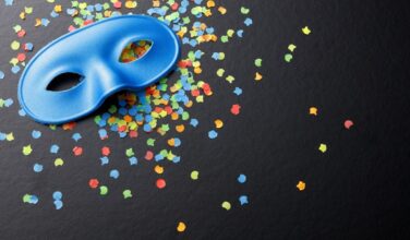 Venetiaans masker (blauw), liggend op een zwarte achtergrond op veelkleurige confettie