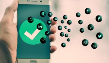 Een hand houdt een smartphone omhoog. Er staat een grote groene vink in een cirkel in het scherm en er komen allemaal bubbels met het logo van een applicatie uit de telefoon