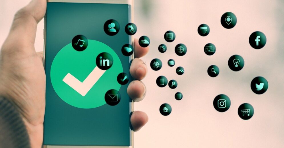 Een hand houdt een smartphone omhoog. Er staat een grote groene vink in een cirkel in het scherm en er komen allemaal bubbels met het logo van een applicatie uit de telefoon