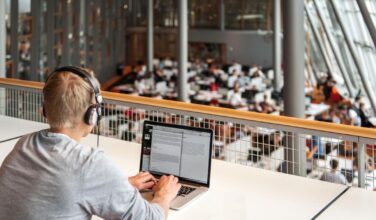 student met koptelefoon op eerste verdieping aan een tafel met uitzicht op de verdieping eronder