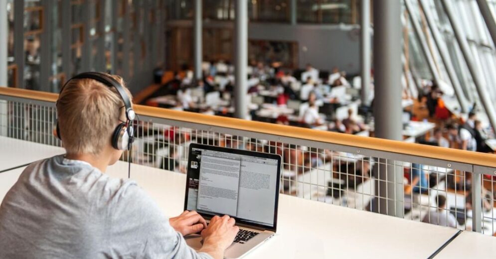 student met koptelefoon op eerste verdieping aan een tafel met uitzicht op de verdieping eronder