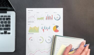 Laptop en uitdraai met analyse van data met rechtsonder een notitieblokje en een hand daarop, passend bij data-ethiek in de sector onderwijs en onderzoek